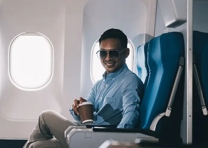 a Man in a blue shirt sitting by an flight window, holding a coffee cup