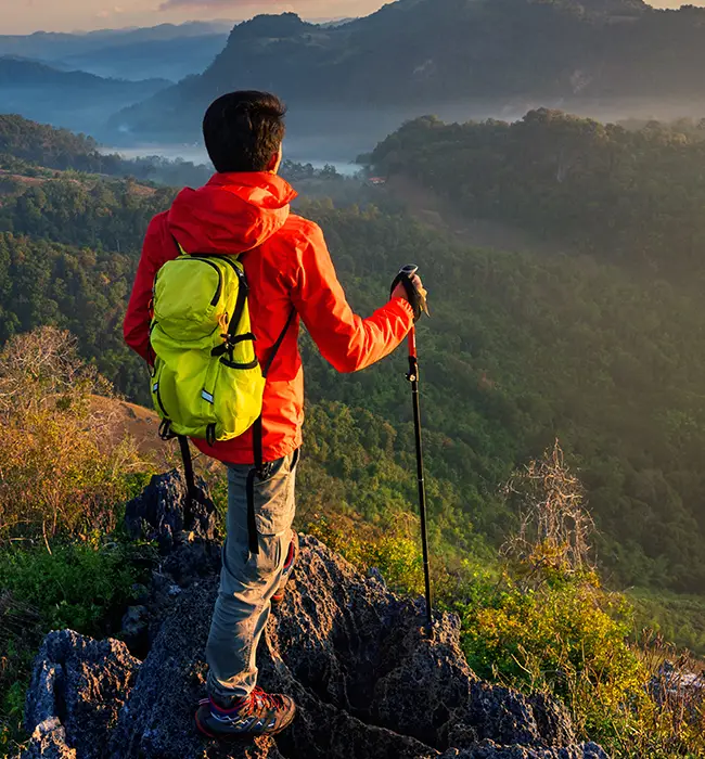 a traveler in red jacket with backpack standing on a mountain summit at dawn
