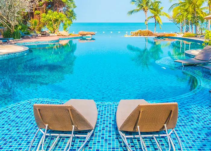 a hotel with Infinity pool with sun loungers overlooking a tropical beach
