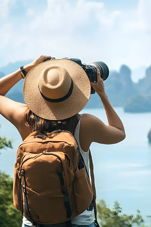 a lady traveler with a hat and backpack taking a photo of a scenic landscape