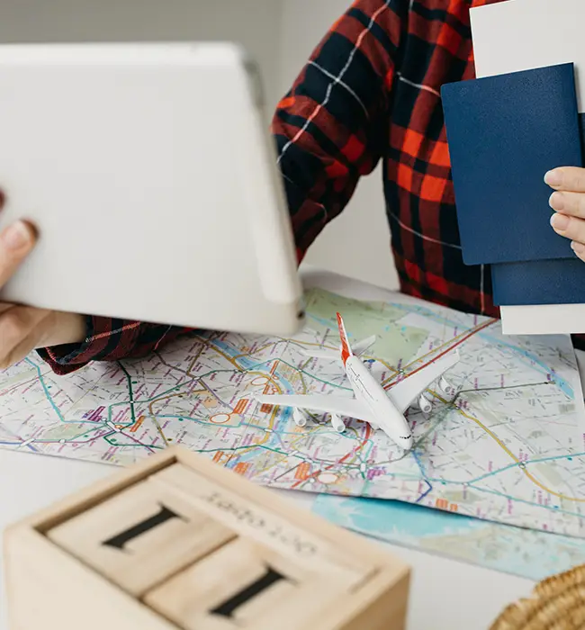 a person holding a tablet and passport over a map with a toy airplane and clocks booking fligt through travel agency