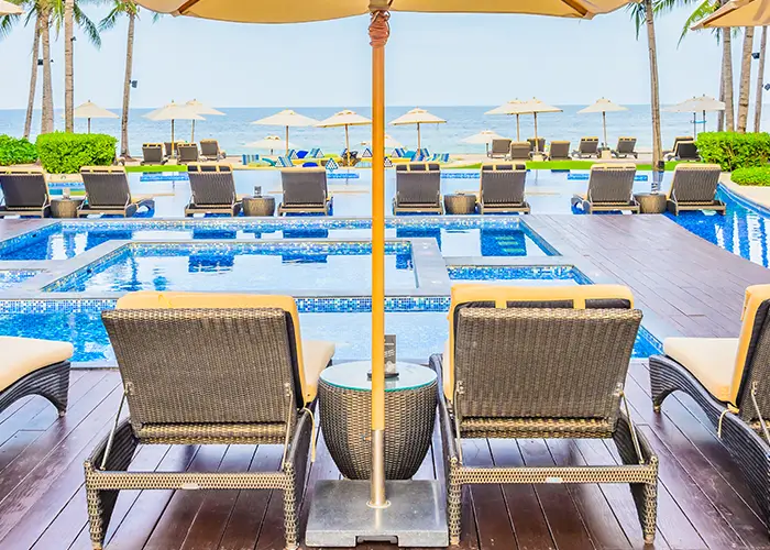 Luxury poolside lounge area with chairs and umbrellas by the sea.