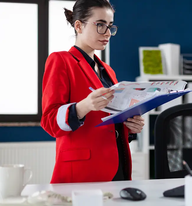 a travel agent in red blazer holding documents in an office setting.