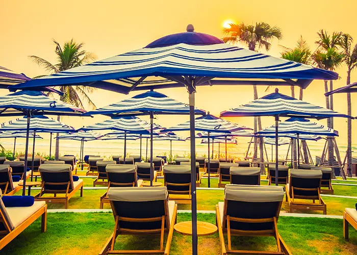 Beach resort with striped blue and white umbrellas, lounge chairs, and palm trees at sunset