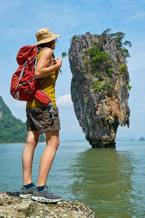 Traveler with backpack admiring a tall limestone karst in the sea.
