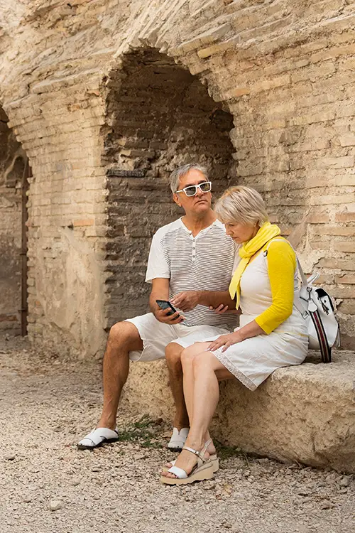 Two people sitting on an ancient stone bench by a brick wall, one holding a smartphone