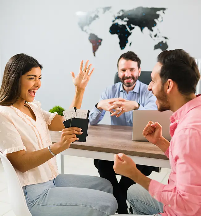 Three people at a table with one person gesturing, another with a laptop, and a world map in the background of a travel agency.