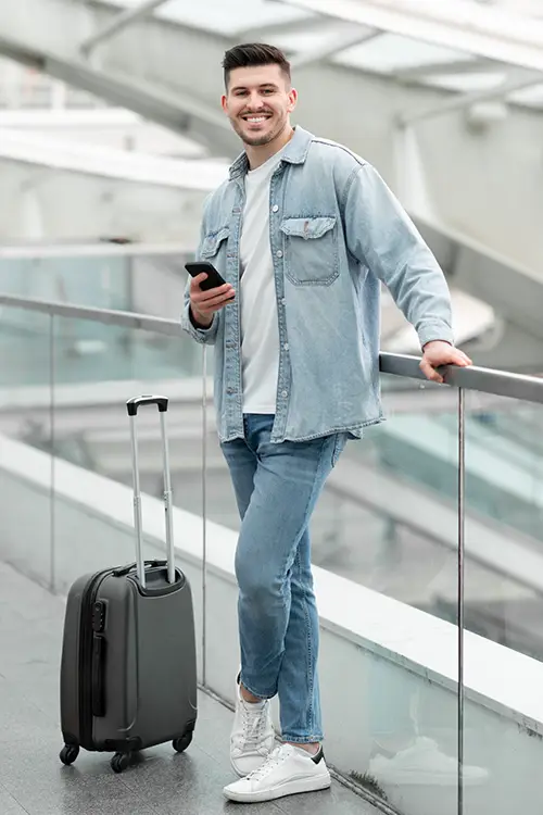 a happy traveller holding mobile and luggage nearby