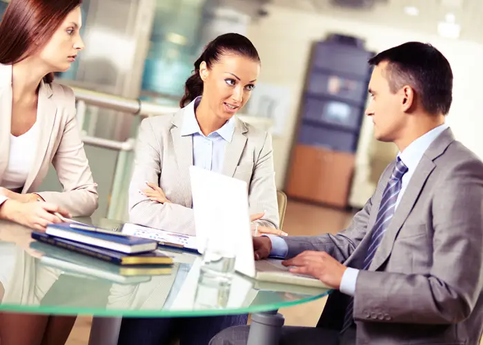 Three professionals in a meeting at a glass table with documents.