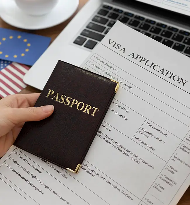 Hand holding a passport over a visa application form with a laptop and EU flag in the background.