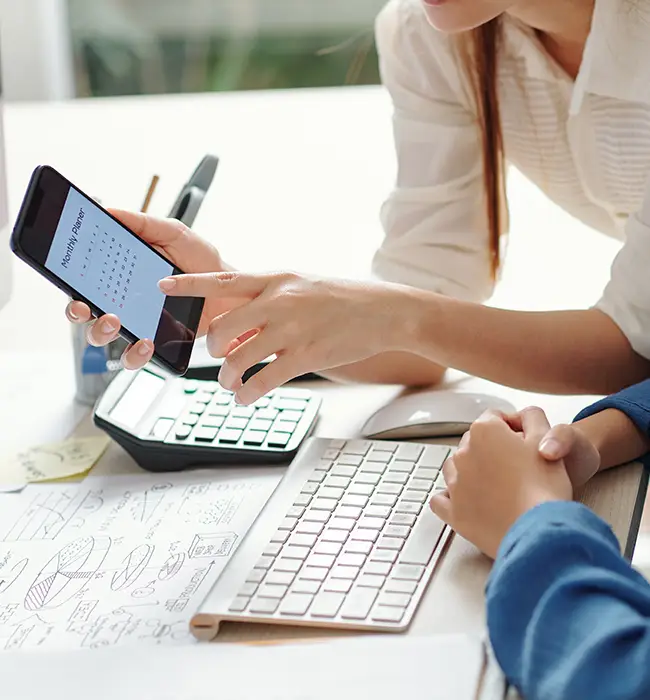 Person holding smartphone with calendar on screen over a business desk setting.