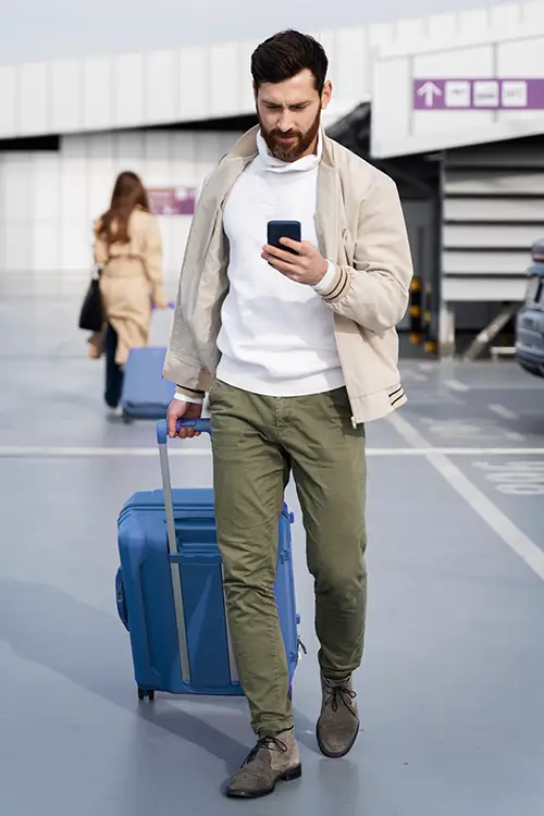 handsome young traveller with trolley bag and mobile in the airport